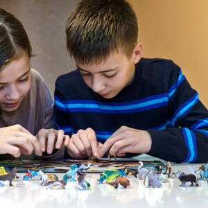 May include: Two children are working on a puzzle with colorful animal figurines. The puzzle is spread out on a white table. The children are focused on the task at hand.