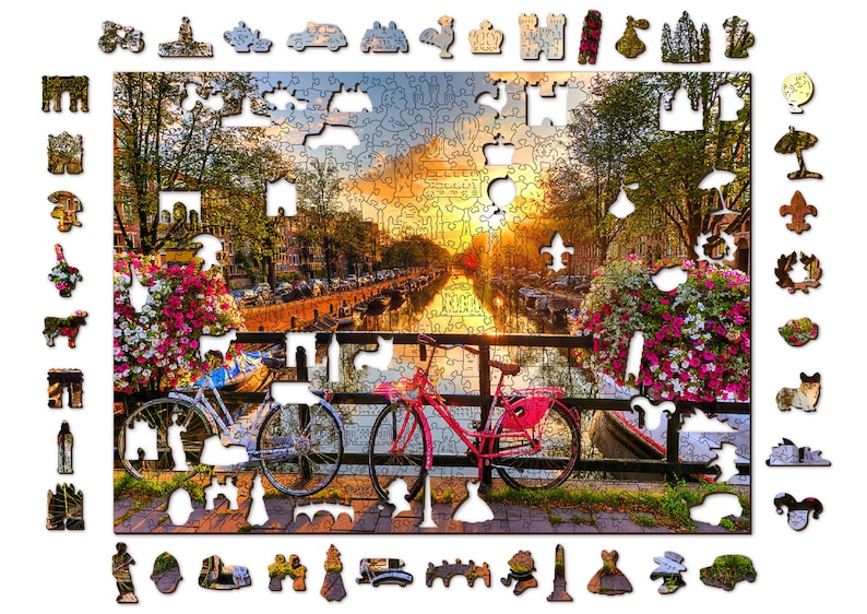May include: A colorful jigsaw puzzle depicting a canal scene in Amsterdam, Netherlands. The puzzle features a bridge with two bicycles parked on it, a canal with boats, and buildings along the canal. The sky is a vibrant orange and pink, and there are flowers in bloom along the canal.