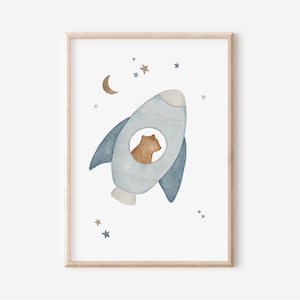 Könnte beinhalten: Aquarellillustration eines Bären in einer hellblauen Rakete, umgeben von Sternen und einem Mond. Das Kunstwerk ist in einem hellen Holzrahmen gerahmt, ideal für ein Kinderzimmer.