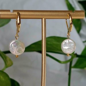Op de afbeelding: Een paar gouden creolen met een witte parel hanger aan elke oorring.