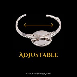May include: Silver adjustable ring with a round, silver-toned center piece. The ring is adjustable and the text "ADJUSTABLE" is printed below the ring.