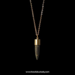 Puede incluir: Un collar de cadena dorada con un colgante de bala de color gris oscuro. El colgante tiene una parte superior e inferior doradas.