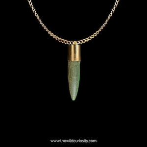 Puede incluir: Un collar de cadena dorada con un colgante de bala verde. La bala est&aacute; hecha de un material verde y tiene una parte superior dorada.