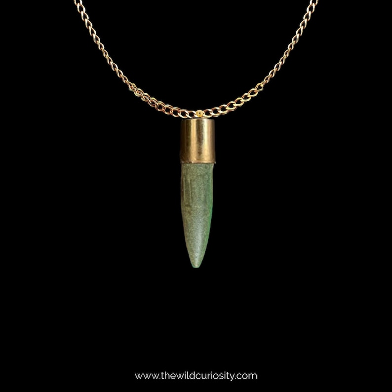 Puede incluir: Un collar de cadena dorada con un colgante de bala verde. La bala est&aacute; hecha de un material verde y tiene una parte superior dorada.