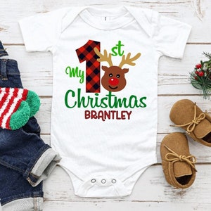 May include: White baby onesie with a red and black plaid number one, a red-nosed reindeer, and the text "My 1st Christmas Brantley".