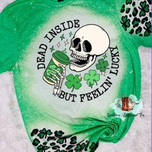 May include: Green and white bleached t-shirt with a skull holding a coffee cup and the text "Dead inside but feelin' lucky". The shirt has a green shamrock pattern on the sleeves.