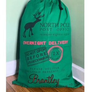 May include: Green Santa sack with a reindeer graphic and the text "North Pole Post Office" and "Overnight Delivery". The sack also has a red and white stamp that says "Do Not Open Before 25 December" and another red and white stamp that says "2X". The sack is personalised with the name "Brantley".