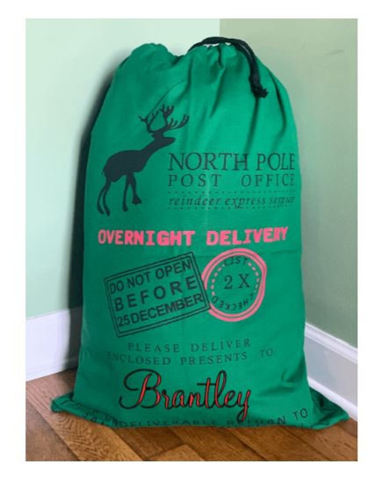 May include: Green Santa sack with a reindeer graphic and the text "North Pole Post Office" and "Overnight Delivery". The sack also has a red and white stamp that says "Do Not Open Before 25 December" and another red and white stamp that says "2X". The sack is personalised with the name "Brantley".