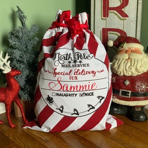 May include: Red and white striped Christmas stocking with a black and white label that says "North Pole Mail Service Special Delivery For Sammie Naughty Nice".