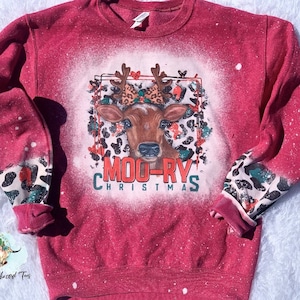May include: Red sweatshirt with a bleached design of a cow with antlers wearing a bow. The design includes the text "Moo-ry's Christmas" and a leopard print pattern.