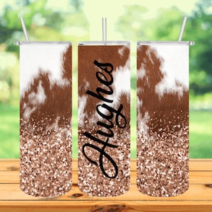 May include: Three stainless steel tumblers with a brown and white cowhide pattern and rose gold glitter. The middle tumbler has the name "Hughes" written in black on the side.