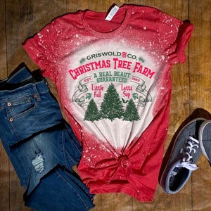 May include: Red and white bleached t-shirt with a distressed vintage design. The text reads "Griswold Co. Christmas Tree Farm Est. 1989 A Real Beaut Guaranteed Little Full Lotta Sap".