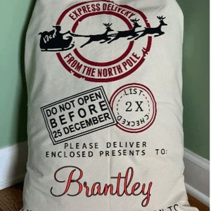 May include: A white canvas Santa sack with black and red text that reads "Express Delivery from the North Pole".  It also has a black and red graphic of Santa's sleigh with reindeer.  The text "Do Not Open Before 25 December" is printed in black and red.  The text "Please Deliver Enclosed Presents To: Brantley" is printed in black and red.  The text "Undelieverable Return To Santa Claus, North Pole" is printed in black and red.