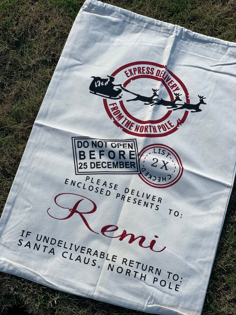 May include: White canvas Santa sack with red and black print. It says "Express Delivery from the North Pole" and "Do Not Open Before 25 December". It also says "Please Deliver Enclosed Presents To: Remi" and "If Undeliverable Return To: Santa Claus, North Pole".