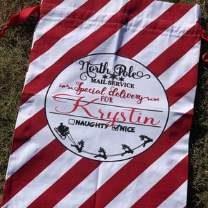 May include: Red and white striped Christmas gift bag with a circle design that says "North Pole Mail Service Special Delivery for Krystin" with a checkbox for "Naughty" and a checkmark for "Nice".