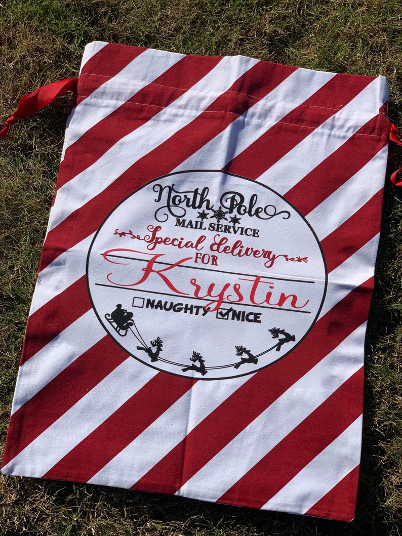 May include: Red and white striped Christmas gift bag with a circle design that says "North Pole Mail Service Special Delivery for Krystin" with a checkbox for "Naughty" and a checkmark for "Nice".