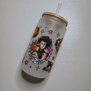 May include: A frosted glass tumbler with a bamboo lid and a clear straw. The tumbler features a colorful graphic print of a couple from the movie "Edward Scissorhands" with a heart, flowers, and stars.