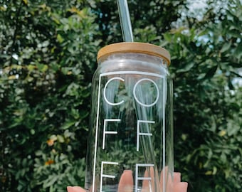 Può includere: Una bottiglia d'acqua riutilizzabile in vetro trasparente con un tappo in bambù e una cannuccia di vetro. La bottiglia ha la scritta "COFFEE" stampata in bianco.