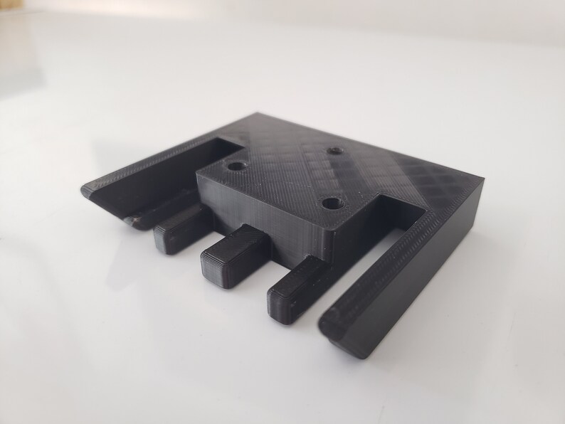 May include: Black plastic 3D printed part with three slots and four holes.