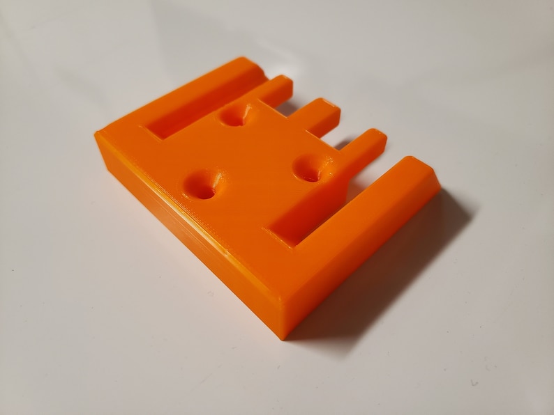 May include: Orange plastic 3D printed object with four slots and three holes.