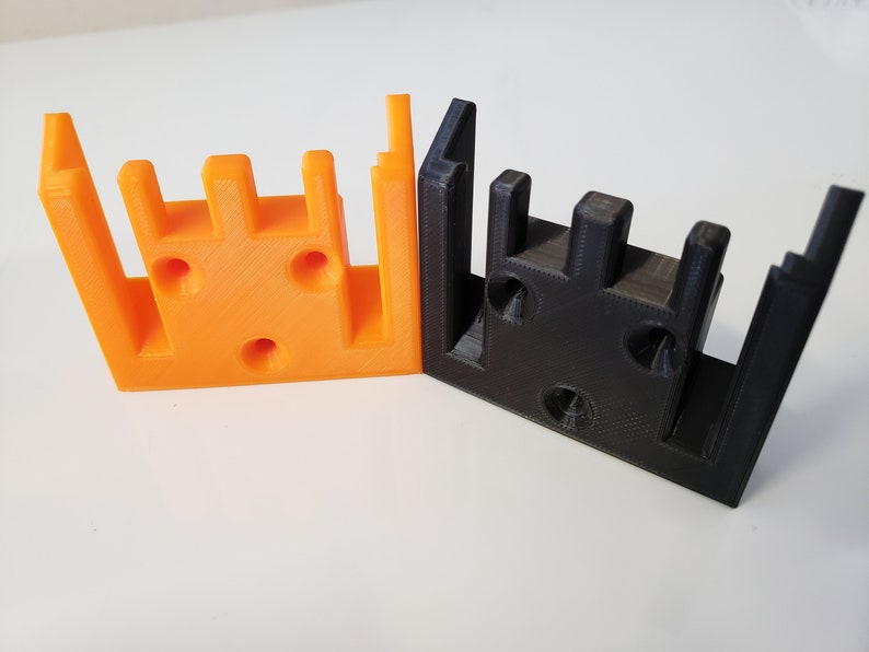 May include: Two 3D printed plastic pieces, one orange and one black, with multiple holes and slots. The pieces are designed to fit together.
