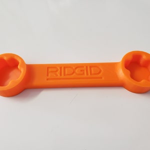 May include: An orange plastic wrench with the word "RIDGID" embossed on the handle. The wrench has two ends, each with a different size star-shaped opening.