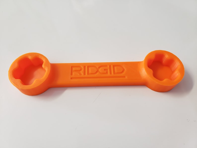 May include: An orange plastic wrench with the word "RIDGID" embossed on the handle. The wrench has two ends, each with a different size star-shaped opening.