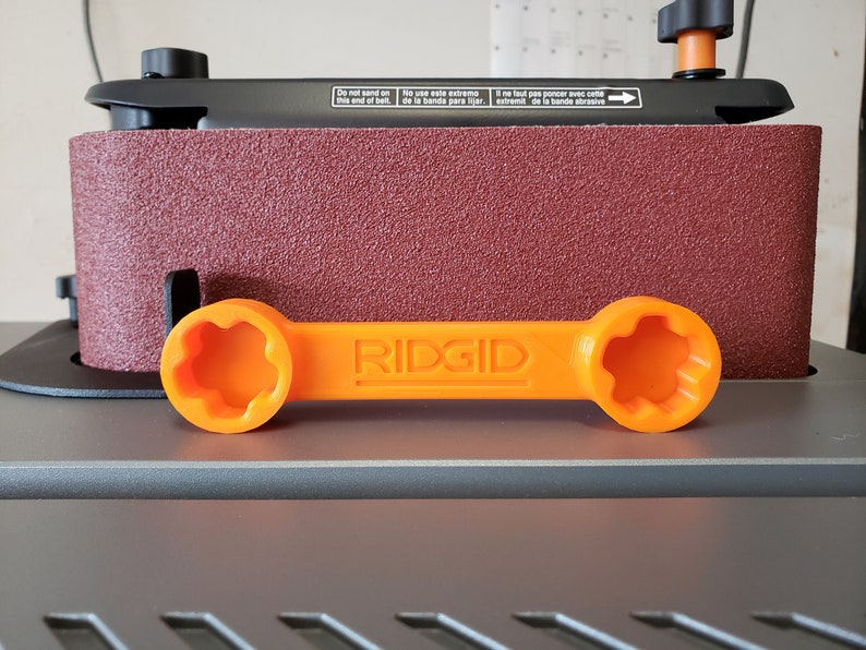 May include: Orange plastic wrench with the word "RIDGID" printed on it. The wrench has a star-shaped opening on each end.