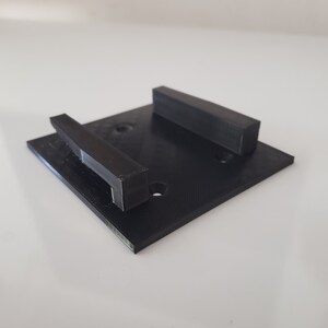 May include: A black plastic wall mount with two rectangular slots. The mount has four small holes for screws.