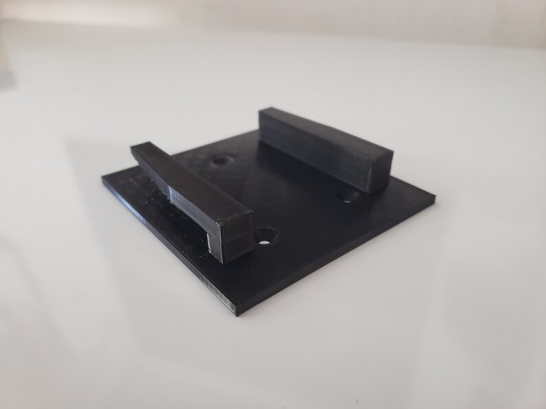 May include: A black plastic wall mount with two rectangular slots. The mount has four small holes for screws.