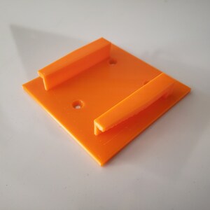 May include: Orange plastic wall mount with two slots for holding objects.