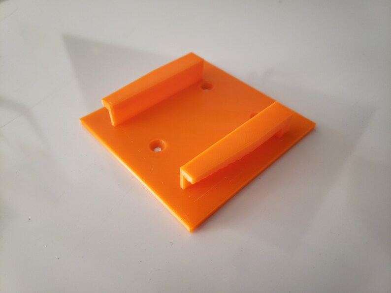 May include: Orange plastic wall mount with two slots for holding objects.