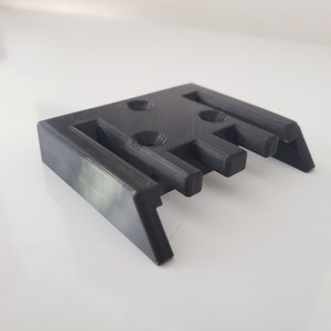 May include: A 3D printed black plastic bracket with four holes and five slots.