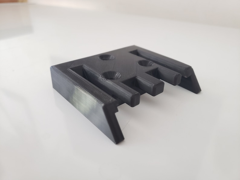 May include: A 3D printed black plastic bracket with four holes and five slots.