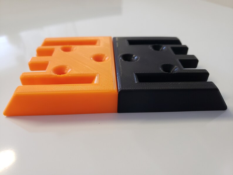 May include: Two 3D printed blocks, one orange and one black, with multiple holes and slots. The blocks are side by side.