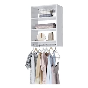 Op de afbeelding: Een witte, aan de muur gemonteerde kastorganizer met planken en een kledingroede. De planken bevatten een draadmand, gevouwen linnengoed en decoratieve dozen. Verschillende kledingstukken hangen aan de roede, waaronder shirts en jurken.
