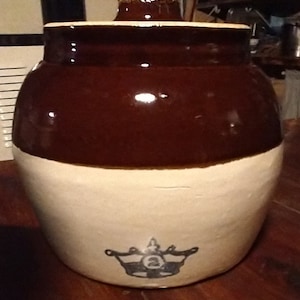 Puede incluir: Un tarro de cerámica esmaltado marrón y blanco con tapa. El tarro tiene una corona negra con el número 2 en su interior.