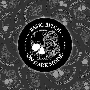Puede incluir: Diseño gráfico en blanco y negro de una calavera con flores en un lado. El texto "Basic Bitch On Dark Mode" está escrito en un círculo alrededor de la calavera.