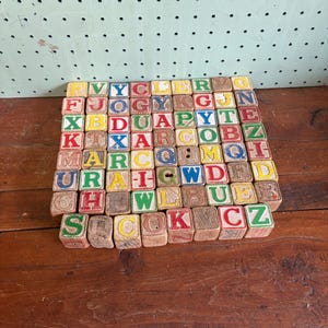 May include: A collection of vintage wooden alphabet blocks, each with a different letter in various colors. The blocks are arranged on a wooden surface, showcasing a classic educational toy.