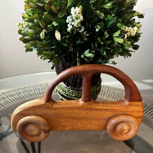 May include: A wooden toy car with brown and natural wood tones. The car has a rounded shape and large wheels.
