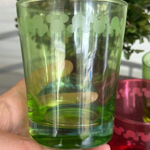 May include: A green glass drinking glass with a white Mickey Mouse design around the top edge.