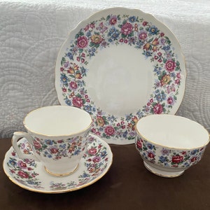 Puede incluir: Un juego de té vintage floral, que incluye una taza de té y un platillo, y un plato para pasteles. La taza de té y el platillo tienen un fondo blanco con un delicado patrón floral en tonos de rosa, azul y verde. El plato para pasteles tiene un fondo blanco con un borde floral en tonos de rosa, azul y verde.