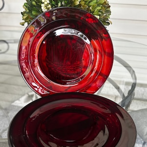 Può includere: Due piatti di vetro rosso scuro con un bordo rialzato e un pozzetto centrale. I piatti sono impilati uno sopra l'altro.