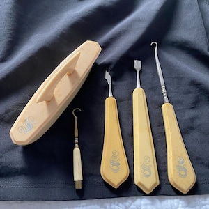 Peut inclure: Un ensemble de cinq outils de manucure, comprenant une lime à ongles, un pousse-cuticules, un coupe-ongles et deux pinces à épiler. Les outils sont en bois et ont une couleur brun clair.