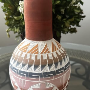 May include: A hand-painted ceramic vase with a Southwestern design. The vase is white with brown, orange, pink, and blue geometric patterns.