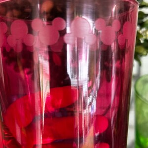 May include: A pink glass with a Mickey Mouse design. The glass is filled with a red liquid.