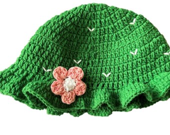 May include: Green crocheted sun hat with a pink flower accent. The hat has a wide brim and a ruffled edge.