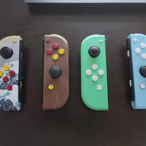 May include: Four different Nintendo Switch Joy-Con controllers. The controllers are in various colors and designs, including a white and blue controller with a wave pattern, a brown wooden controller, a light green controller, and a light blue controller.