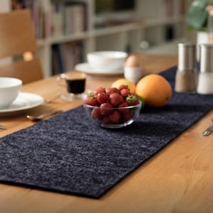 May include: A dark blue felt table runner on a wooden table. A clear glass bowl of strawberries, an orange, and a cup of coffee are on the table. Salt and pepper shakers are also visible.