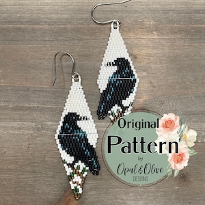 May include: Handmade beaded earrings with a black and white bird design. The earrings have a teardrop shape with a white background and a detailed raven illustration. They are finished with silver-tone ear wires.